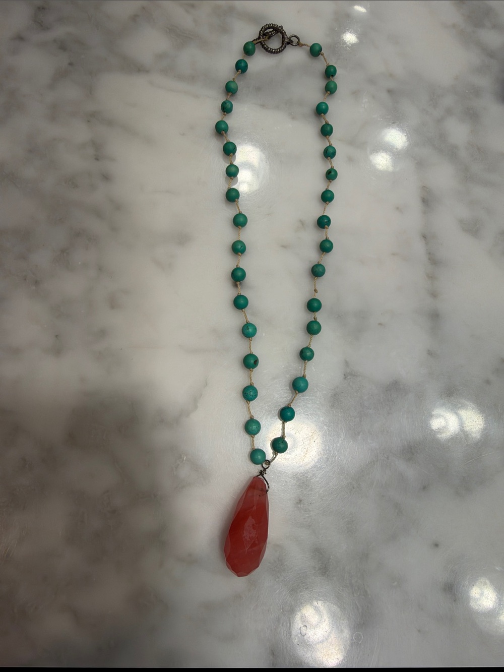 A hand-knotted, genuine turquoise necklace featuring a cherry quartz pendant